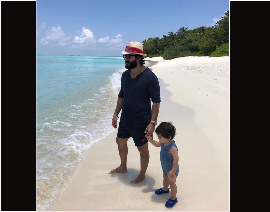 বাবার সঙ্গে সমুদ্র সৈকতে হাত ধরে দাঁড়িয়ে রয়েছে খুদে নবাব। দু’জনের পরনেই নীল।