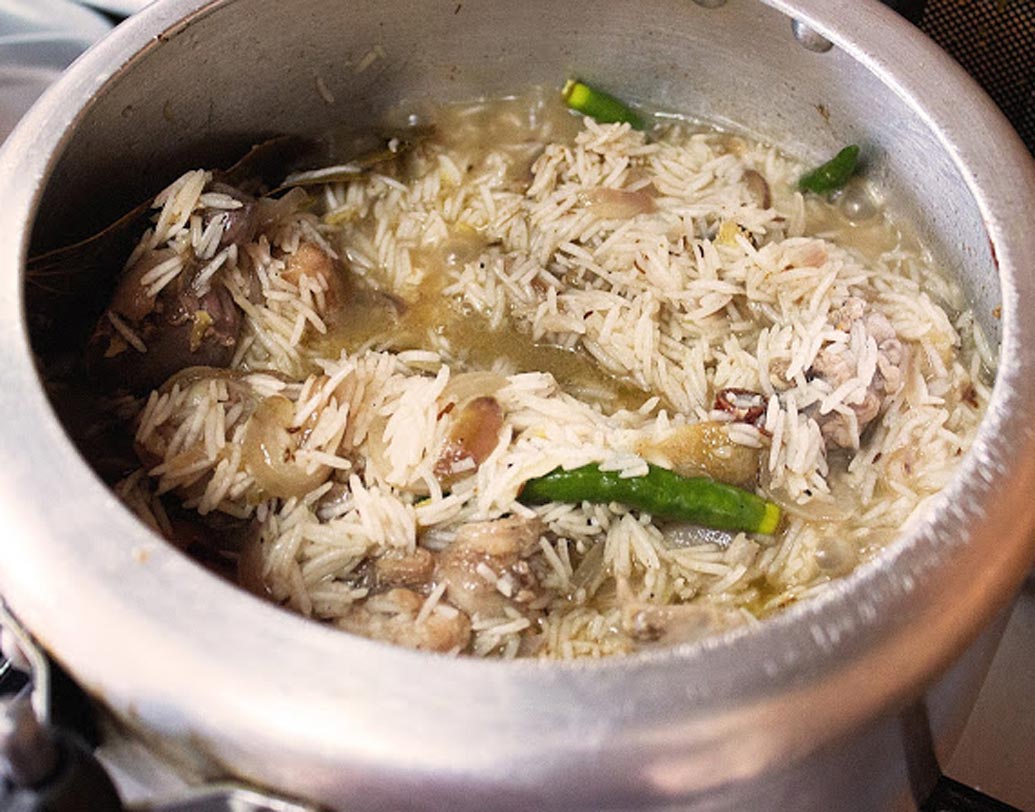 নুন, ২ চা চামচ বিরিয়ানি মশলা, বাকি গোলাপ জল, কেও়ড়া জল, মিঠা আতর দিয়ে দিন। এরপর চেরা কাঁচা লঙ্কা দিয়ে প্রেশার কুকারের ঢাকনা বন্ধ করে মাঝারি আঁচে ১টা হুইসল ওঠা পর্যন্ত রান্না করুন।