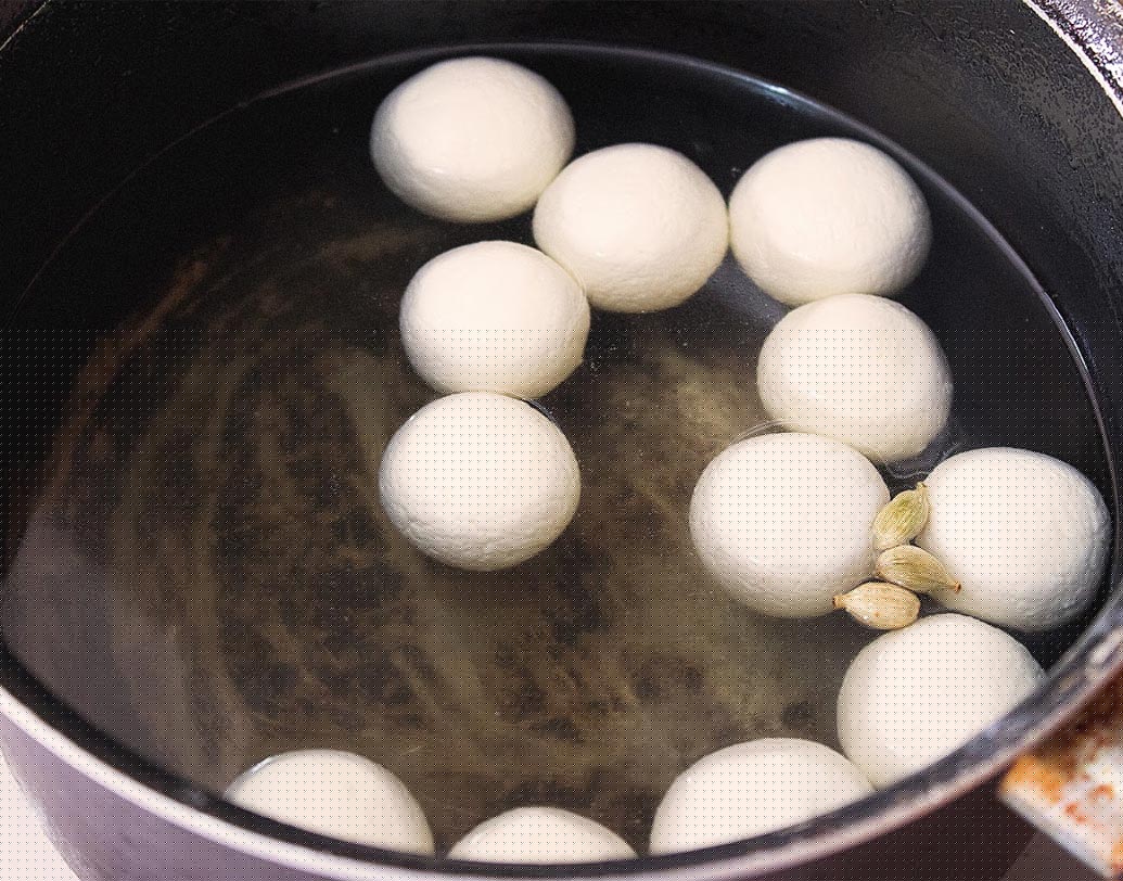 ১টা সসপ্যানে জল গরম করুন। এলাচ দিয়ে জল ফুটতে দিন। এর মধ্যে ছানার বল দিয়ে ফোটাতে থাকুন যতক্ষণ না বলগুলো ফুলে দ্বিগুণ আকারের হচ্ছে ও ভাসতে শুরু করছে। জল থেকে তুলে রসগোল্লা চিপে জল বের করে রাখুন।