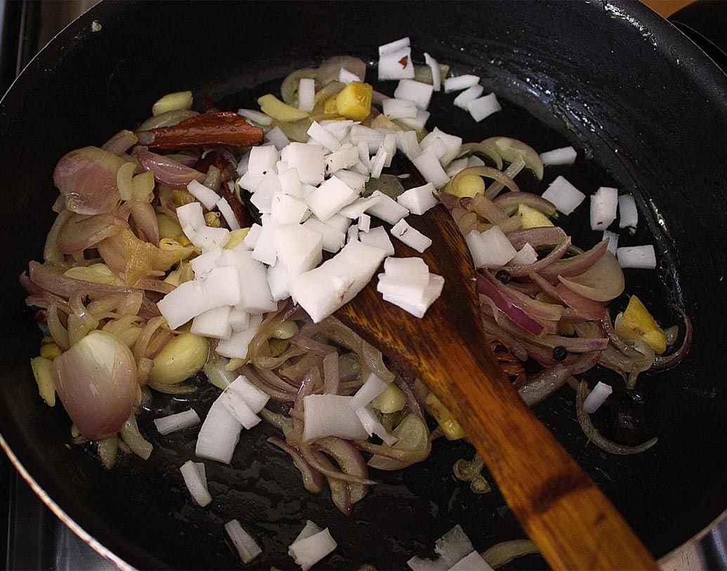 পেঁয়াজ বাদামি রং ধরতে শুরু করলে কুচনো নারকেল দিয়ে আরও ২-৩ মিনিট নেড়ে নিন। এর সঙ্গে অর্ধেক ধনেপাতা ও সামান্য জল দিয়ে মিহি করে বেটে নিন।