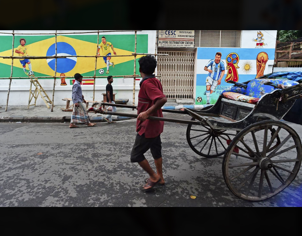 আলিপুরের গোপালনগরে দেওয়ালে আগেই শুরু হয়ে গিয়েছে বিশ্বকাপ। বল পায়ে দৌড়চ্ছেন মেসি-নেমাররা। মুগ্ধ বিস্ময়ে তাকিয়ে রিকশাচালক। এই এক মাস পুরো বিশ্বও অপলক তাকিয়ে থাকবে মেসির জাদুর দিকে, নেমারের সাম্বা-ঝলকের দিকে। দু’জনেই চাপে। নেমার চোট সারিয়ে উঠছেন। আর মেসিকে ঘিরে প্রত্যাশার পারদ চড়ছে।