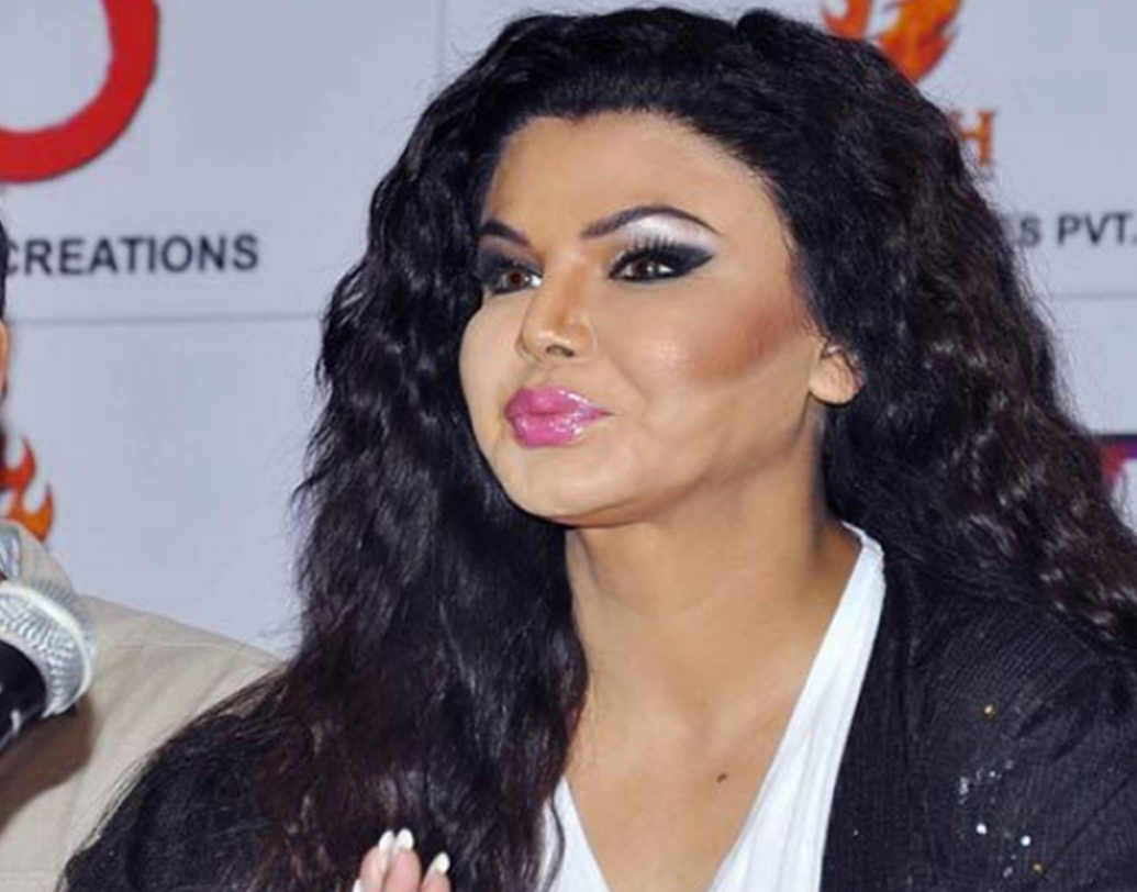 বলিউড ব্লান্ডার হবে আর রাখি সবন্ত থাকবেন না, তা-ও কখনও হয় নাকি! একটি অনুষ্ঠানের মঞ্চে তাঁকে দেখা গিয়েছিল এ ভাবেই। গোলাপি লিপস্টিক আর চড়া মেকআপ নেওয়া রাখিকে দেখে মনে হচ্ছিল যেন, একটা মুখোশ এঁটে রয়েছেন মুখে।