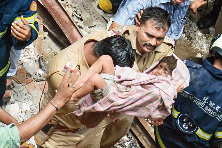 ত্রাতা: ভেঙে পড়া বহুতল থেকে এক শিশুকে উদ্ধার করছেন দমকলকর্মীরা। মঙ্গলবার মুম্বইয়ে। ছবি: পিটিআই