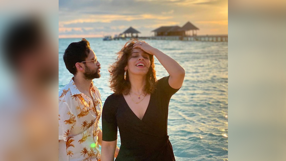 হট গাউনে ধরা দিলেন সাইনা। চোখে সূর্যাস্তের আভা আর মুখে এসে পড়া এলোমেলো চুল। সানকিসড সাইনার পিছনেই কোকোনাট ট্রি প্রিন্ট বিচ শার্টে কাশ্যপ।