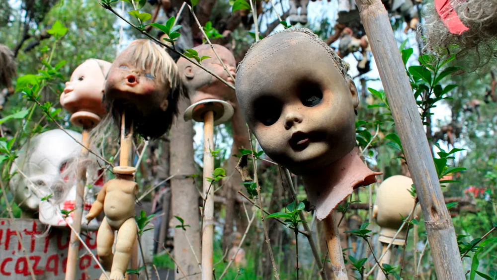 কেউ মুণ্ডহীন, কারও হাত-পা কাটা, কারও আবার সারা শরীর যেন কেউ ছিঁড়ে নিয়েছে। যতদূর চোখ যাবে এই দৃশ্যই চোখে পড়বে। ঘোর কাটলে বুঝতে পারবেন, ওগুলো আসলে পুতুল। সব গাছ থেকেই ঝুলছে ছোট-বড় এমন নানা চেহারার পুতুল।