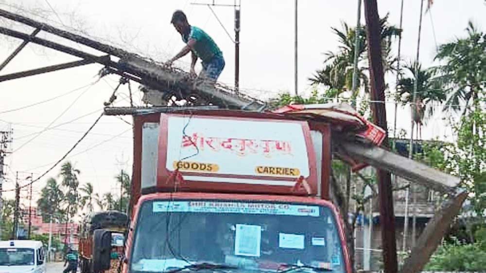 গাড়ির মাথায় ভেঙে পড়েছে বিদ্যুতের খুঁটি। —নিজস্ব চিত্র