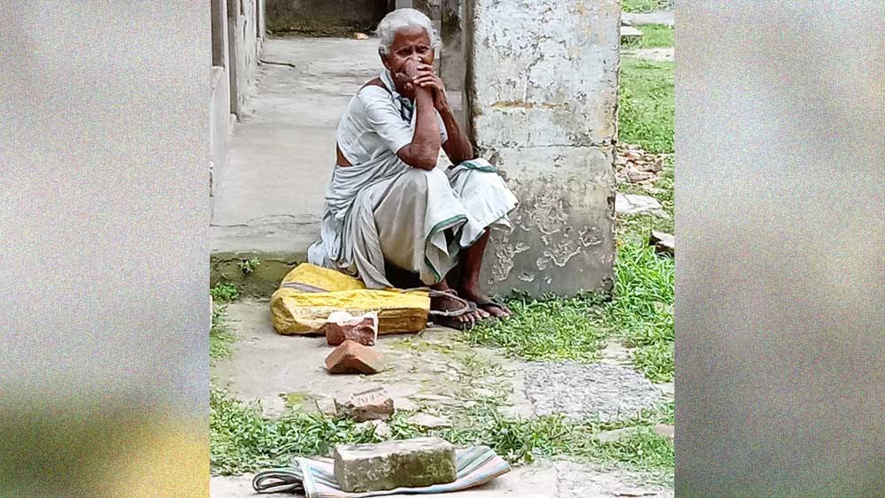 কালনায় রেশন পাওয়ার জন্য অপেক্ষার লাইনে বসে রয়েছেন এক বৃদ্ধা। ছবি: জাভেদ আরফিন মণ্ডল
