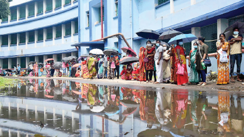 দুর্ভোগ: বালুরঘাট হাসপাতালে বৃষ্টির জমা জলের মধ্যেই ভ্যাকসিন নিতে লাইন। 