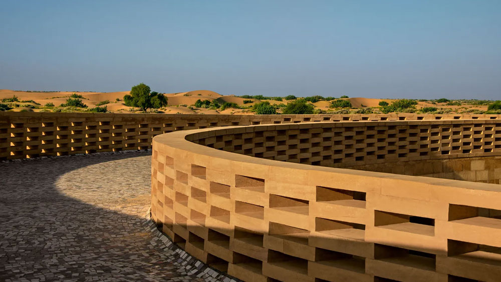 স্কুলটির বাইরের দিকের দেওয়ালে কোনও জানলা নেই। সমস্ত জানলাই ভিতরের মাঠের দিকে। তাই হাওয়ার সঙ্গে বালি উড়ে স্কুলের ভিতরে ঢোকার উপায় নেই।