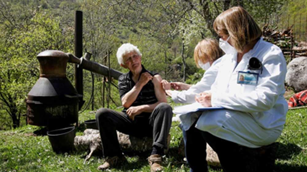 ইউরোপের বালকানস-এর মন্টেনেগ্রোর কোলাসিন পুরসভা দরজায় দরজায় টিকা নিয়ে পৌঁছে যেতে শুরু করেছে। এই পুরসভার অন্তর্গত এক গ্রামে এ ভাবেই খোলা আকাশের নীচে টিকা নিচ্ছেন এক ইচ্ছুক ব্যক্তি। পাশেই তৈরি হচ্ছে দেশি মদ।