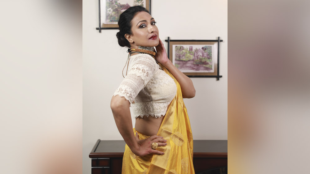 ক্রিম ছেড়ে এবার হালকা হলুদ শাড়ি। সঙ্গে সাদা ব্লাউজ। ঠোঁটে গাঢ় লাল লিপস্টিক, চোখে ধূসর রঙের পরত। গাঢ় হল চোখের ভাষা। শাড়ির হলুদ ততক্ষণে মিলেমিশে গিয়েছে সোনারং ত্বকে।