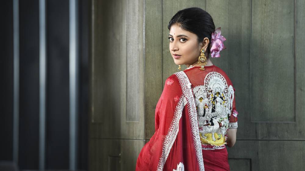 শাড়ির মতোই নজরকাড়া সঙ্গে ব্লাউজটাও। দুর্গাপুজোর মণ্ডপ ধরা পড়েছে ব্লাউজের কারুকাজে। একচালা প্রতিমার শোলার সাজের ছোঁয়া রয়েছে সন্দীপ্তার শাড়ি ও ব্লাউজে।