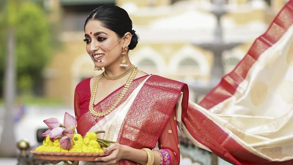 গরদের লাল-পাড় সাদা শাড়িতে নজরকাড়া ইশা সাহা। সোনার গয়না, নাকে বড় নথ। হাতে ধরা মাটির সরাতে হলুদ গাঁদা, পদ্ম। সাক্ষাত্ দেবী যেন!