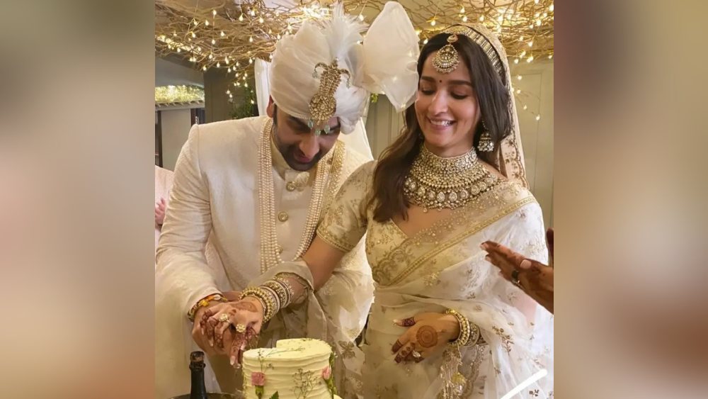 বিয়ে-শাদি শেষ। এ বার পার্টি তো বনতা হ্যায়! রীতি মেনে জম্পেশ ভোজের আগে বর-বউয়ের সামনে দুধ সাদা কেক। গায়ে গোলাপি রঙের বসরাই গোলাপ আঁকা। হাসতে হাসতে তুলতুলে নরম কেকের বুকে মেহেন্দি রাঙা হাতে ছুরি বসিয়েছেন আলিয়া!