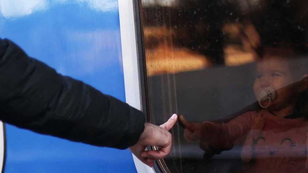 মাঝখানে ব্যবধান কাচের জানালা। বিদায়বেলায় বাবা এবং শিশুসন্তানের আবেগঘন মুহূর্তের ছবি৷ সরকারি নির্দেশ, দেশে থাকতে হবে পুরুষদের। এর পর পরিবারকে নিরাপদ স্থানে সরাতে হচ্ছে।