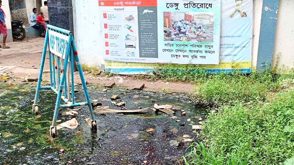 পিছনে টাঙানো ডেঙ্গি নিয়ে সরকারি সচেতনতার বার্তা। সামনে জমে রয়েছে জল-কাদা। যশোর রোডের গায়ে হাবড়া থানায় প্রবেশ পথের সামনে এই অবস্থা বেশ কিছুদিন ধরে। —সুজিত দুয়ারি