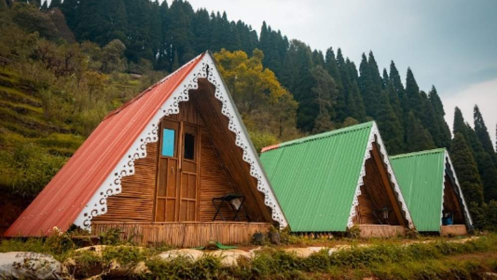 গুরদুম ব্যাকপ্যাকার্স ক্যাম্প: পাকদণ্ডী বেয়ে একটু উপরে উঠতেই, এ যে অন্য জগৎ! পাইন জঙ্গলের সামনে কেবিন ইন দ্য উডস। সামনে মেঘেদের ছোটাছুটি। যেন মেঘের উপরেই দাঁড়িয়ে আছেন আপনি! রাত গড়ালে ওপারের পাহাড়ে দার্জিলিংয়ের আলোগুলো তারার মতো জ্বলে। বাকেট লিস্টে এ সব আছে নাকি? তা হলে ঘুরেই আসুন এই ক্য়াম্পে। কলকাতা থেকে এখানকার দূরত্ব প্রায় ৬৫৮ কিলোমিটার। থাকা, খাওয়া ও ক্য়াম্প ফায়ার নিয়ে মাথাপিছু খরচ পড়বে ১১০০ থেকে ১৩০০ টাকা। ছবি ও তথ্য সৌজন্যে: ইজিফিসো ব্যাকপ্যাকার্স। 