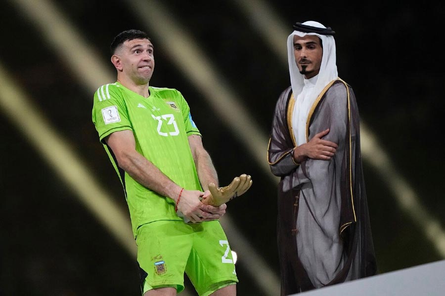 কাতারের মতো গোঁড়া দেশ। সেখানে বিশ্বকাপ ফুটবলের পুরস্কার দেওয়ার মঞ্চে উপস্থিত দেশের রাজা। এমিলিয়ানো মার্তিনেস কি না তাঁর সামনেই দাঁড়িয়ে সদ্য পাওয়া সোনার দস্তানা চেপে ধরলেন দু’পায়ের সংযোগস্থলে! পাগল নাকি— অঙ্গভঙ্গি দেখে ভেবেছিলেন অনেকেই। তবে আর্জেন্টাইন গোলরক্ষককে যাঁরা কাছ থেকে চেনেন, তাঁরা বলছেন তাঁদের প্রিয় ‘ম্যাড ম্যান’ যে এর চেয়েও বড় কোনও পাগলামি করে বসেননি, এই অনেক।