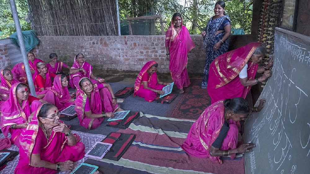  হাতে ব্যাগ নিয়ে গোলাপি শাড়ি পরে দল বেঁধে হেঁটে সকলে স্কুলে যান। 
