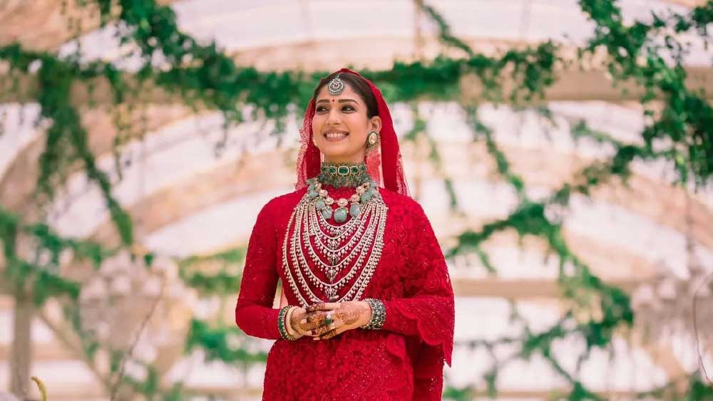 মণিকা জেডের কালেকশন থেকে বিয়ের পোশাক— টুকটুকে লাল শাড়ি বেছে নিয়েছেন নয়নতারা। সঙ্গে সবুজ পাথরের ভারী হার এবং কপালে টিকলি আলাদা মাত্রা দিয়েছে সাজে।