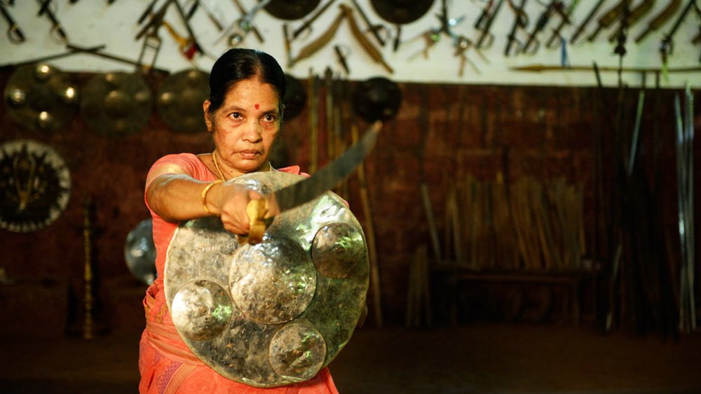 বয়স ৮১ বছর। মুখের চামড়া ঝুলে পড়েছে। কিন্তু দৃষ্টি টানটান। পরনের লালপেড়ে শাড়ির খুঁট কোমরে গোঁজা। বিপক্ষকে চোখ দিয়ে মেপে নিচ্ছেন। এক হাতে তরবারি ঝলসে উঠেছে, অন্য হাতে ঢাল!