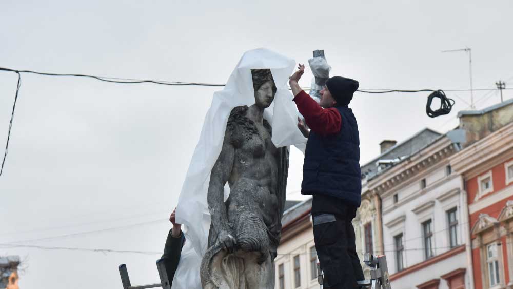 নেটমাধ্যমে দেখা গিয়েছে, বৃহস্পতিবার লুভিভ শহরের সেন্ট্রাল মার্কেট স্কোয়ারে সিঁড়ি নিয়ে নেমে পড়েছেন এক দল ইউক্রেনীয়। শহরের মাঝেই রয়েছে রোমান দেবতা নেপচুন এবং গ্রিক দেবী অ্যামফিট্রাইটির মূর্তি। কারুকাজ করা সেই মূর্তিগুলি প্লাস্টিকের মোটা পরতে মুড়ে ফেলেছেন শহরের বাসিন্দারা। তাতে জড়িয়ে ফেলেছেন সেলোটেপও। 