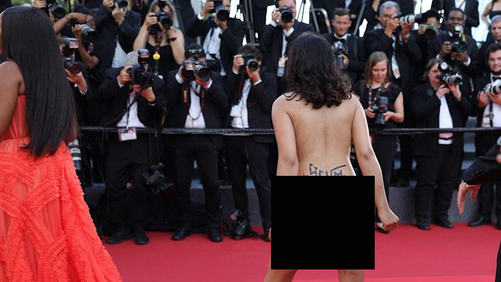 নগ্ন হয়েই গালচের দু’পাশে দাঁড়ানো ফোটোগ্রাফারদের সামনে চলে আসেন তিনি। পরনে ছিল শুধু নিম্নাঙ্গের অন্তর্বাস। তাতে আঁকা ছিল রক্তের দাগ। অনাবৃত ঊর্ধ্বাঙ্গে নীল হলুদ রঙের উপর লেখা ছিল— ‘আমাদের ধর্ষণ কোরো না’।