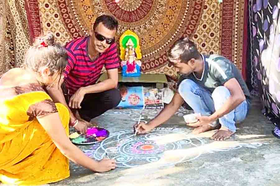 প্রতিমার সামনে আলপনা আঁকছেন সইফুদ্দিন (ডান দিকে)। নিজস্ব চিত্র