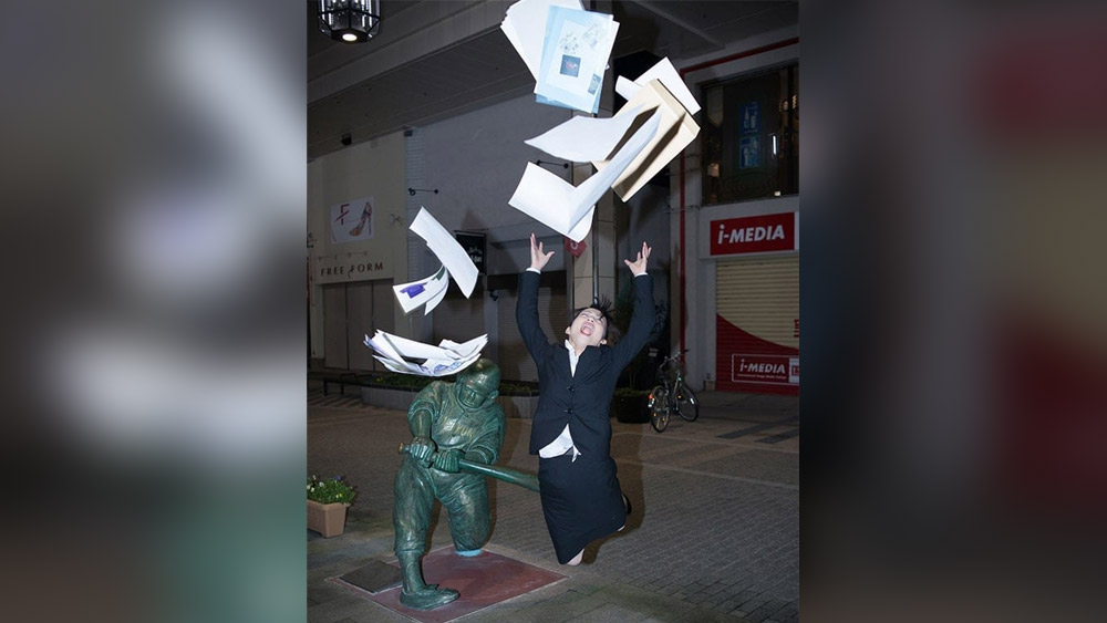 এই মূর্তিটি দেখলে বোঝা যায়, এক খেলোয়াড়ের হাতে ব্যাট ধরানো। কিন্তু মহিলাটি এমন পোজ দিয়েছেন যা দেখে মনে হচ্ছে তিনি জরুরি কাগজপত্র নিয়ে অফিসের কাজে যাচ্ছিলেন। হঠাৎ পিছন থেকে তাঁকে ব্যাট দিয়ে আঘাত করায় তাঁর যেন পড়ে যাওয়ার উপক্রম। আসলে, মূর্তির সঙ্গে ছবি তোলার সময় তিনি উপরের দিকে লাফিয়ে উঠে কাগজপত্রগুলিও শূন্যে ছুড়ে দেন।