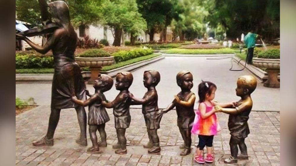 পাশের ছবিতে দেখা যাচ্ছে, এক জন মহিলা কোনও এক বাদ্যযন্ত্র বাজাতে বাজাতে হেঁটে যাচ্ছেন। তাঁর পিছনে ছ’টি বাচ্চা। আসলে, ছ’টির মধ্যে পাঁচটিই পাথরের মূর্তি। দু’টি বাচ্চার মূর্তির মধ্যে কিছুটা দূরত্ব থাকায় মাঝের জায়গাটিতে গোলাপি জামা পরা বাচ্চাটি দাঁড়িয়ে ছবি তুলেছে।