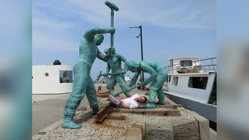 ছবিটিতে তিনটি মূর্তিকে একসঙ্গে একটি লোহার পাত পেটাতে দেখা যাচ্ছে। কিন্তু লোকটি এমন ভাবে ফাঁকের মধ্যে গলে গিয়ে মাটিতে শুয়ে পড়েছেন যে দেখে মনে হচ্ছে, লোহার পাত নয়, বরং লোকটিকেই তিন জন মিলে মারছে।