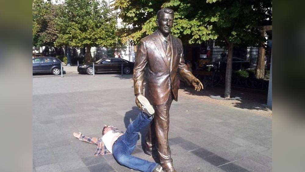 পাশের ছবিটি দেখলে লক্ষ করা যায়, একটি লোক রাস্তার মধ্যে দিয়ে আর একটি লোকের পা ধরে টানতে টানতে নিয়ে যাচ্ছেন। যে লোকটিকে রাস্তা দিয়ে হেঁটে যেতে দেখা যাচ্ছে, সেটি আসলে একটি পাথরের মূর্তি। রাস্তায় শুয়ে থাকা লোকটি মজা করেই এমন ভঙ্গিমায় শুয়ে আছেন যা দেখে মনে হবে, তাঁর পা ধরে টেনে নিয়ে যাওয়া হচ্ছে।