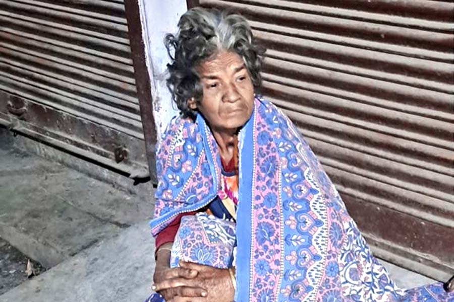 A Photograph of  an old woman sitting on the footpath of a road 