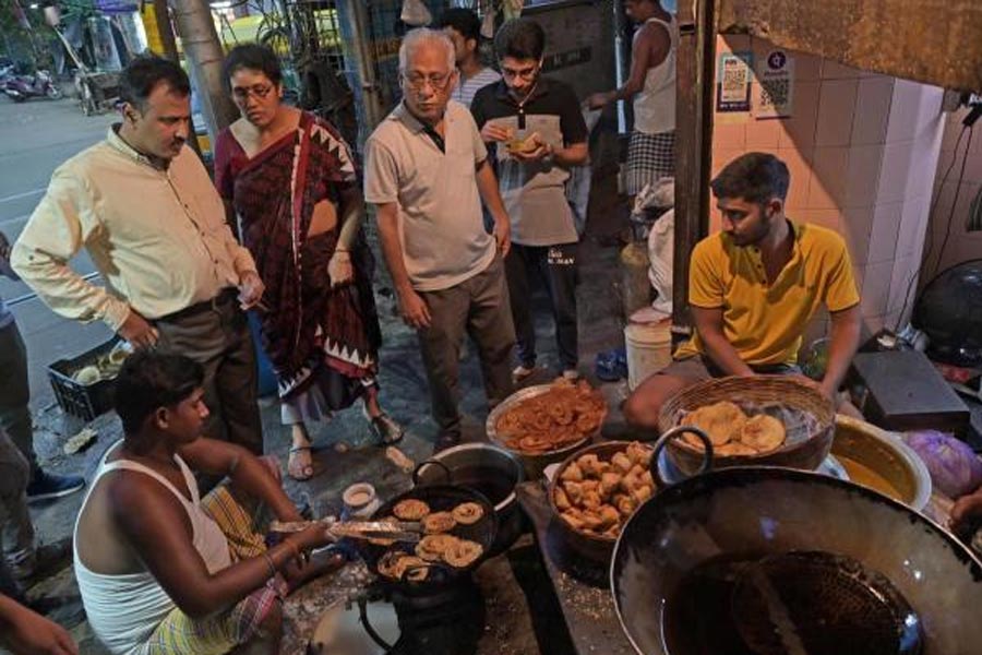 Jilipi Kachuri is being fried in North Kolkata and on the Footpath. people are standing beside oven and eating.