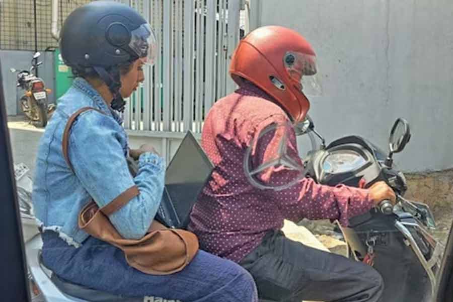 Woman works on Laptop while riding bike in Bengaluru traffic.