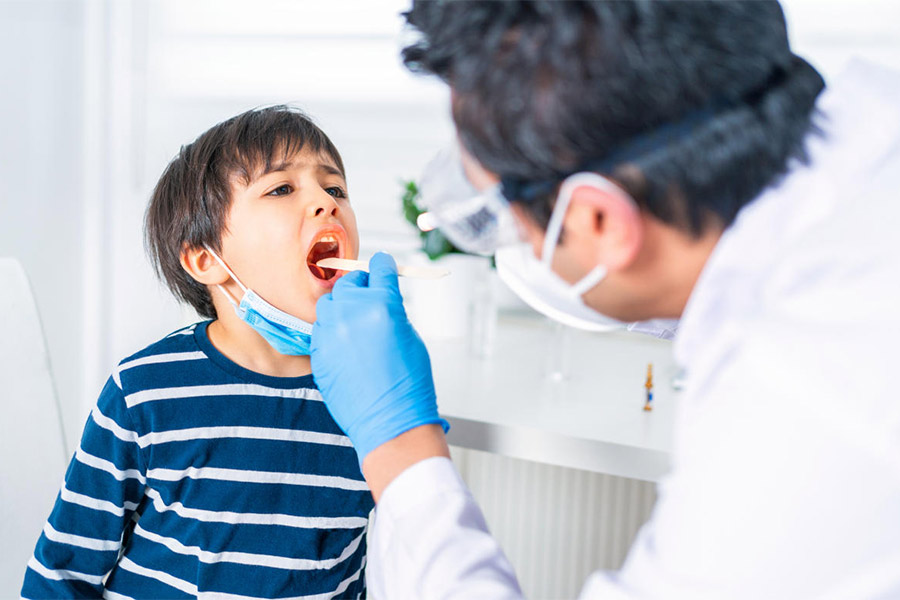 Male pediatrician examining little child patient’s throat at clinic