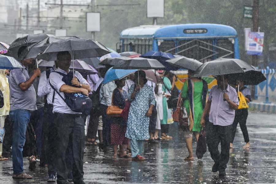 কলকাতার রাস্তায় বৃষ্টি মাথায় নিয়ে দাঁড়িয়ে মানুষ।