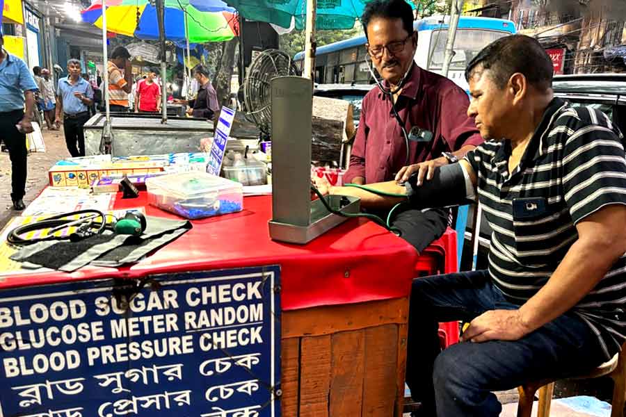 কলকাতার ফুটপাথে বসে রক্তচাপ মাপছেন তপন দাস।