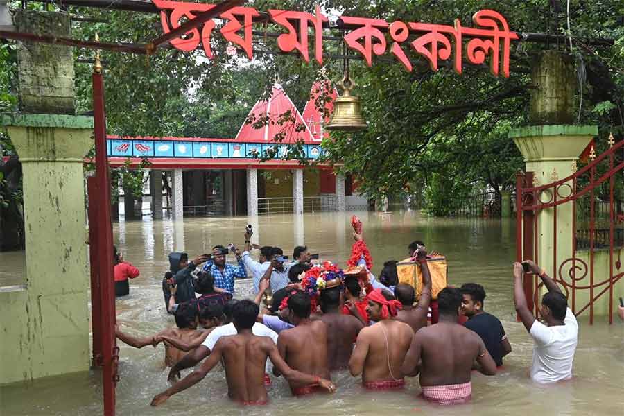 কঙ্কালীতলা মন্দিরে কোপাইয়ের জল । সোমবার কোমর জল ভেঙে ভোগ নিবেদন করতে যাচ্ছেন সেবায়েতরা।