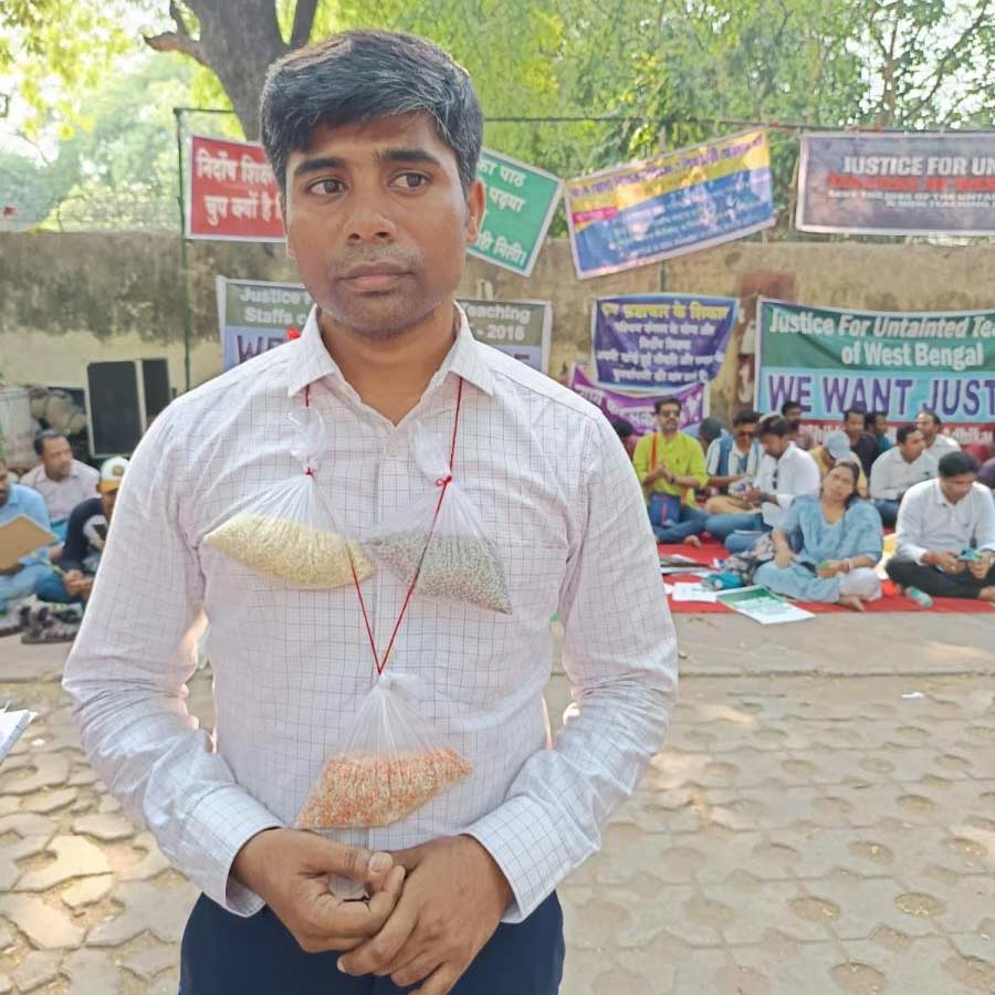 যন্তর মন্তরে চাকরিহারাদের অবস্থানে এক শিক্ষকের গলায় চাল, কালো ডাল ও চালে-ডালে মেশানো থলি। দাবি, চাল-কালো ডালের মতো যোগ্য আর দাগিদের আলাদা করা হোক। বুধবার।