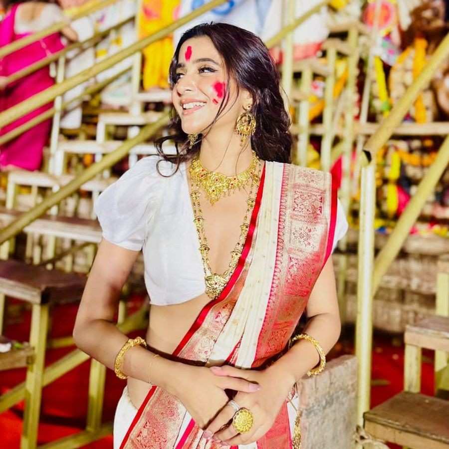 দেবচন্দ্রিমা সিংহ রায়ের সাজ ছিল খানিক জমকালো। সাদা-লাল শাড়ির সঙ্গে আধুনিক ডিজাইনের ব্লাউজ়, আর তার সঙ্গে গলায় চোকার ও লম্বা হার। হাতে চুড়ি, কানে ঝুমকো আর খোলা চুলে ফুটে উঠল উৎসবের প্রাণবন্ত আবহ।