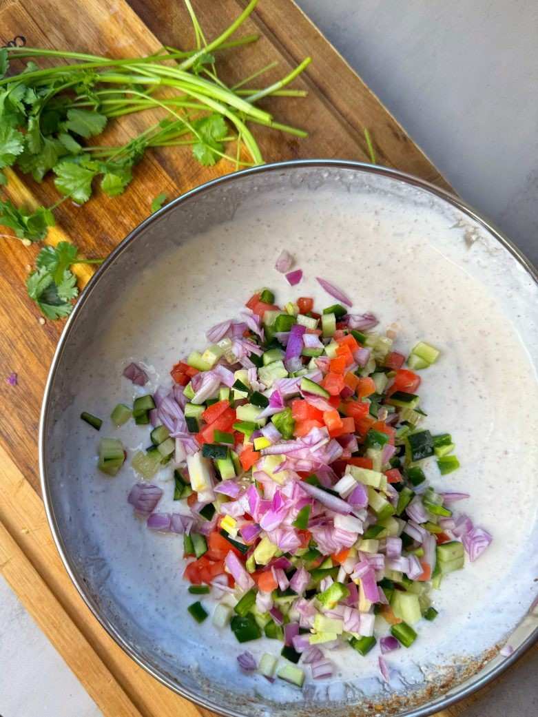 সবজি যোগ করা: দইয়ের মধ্যে কুচোনো পেঁয়াজ, শসা, কাঁচা লঙ্কা, ধনে পাতা এবং পুদিনা পাতা মিশিয়ে নিন।