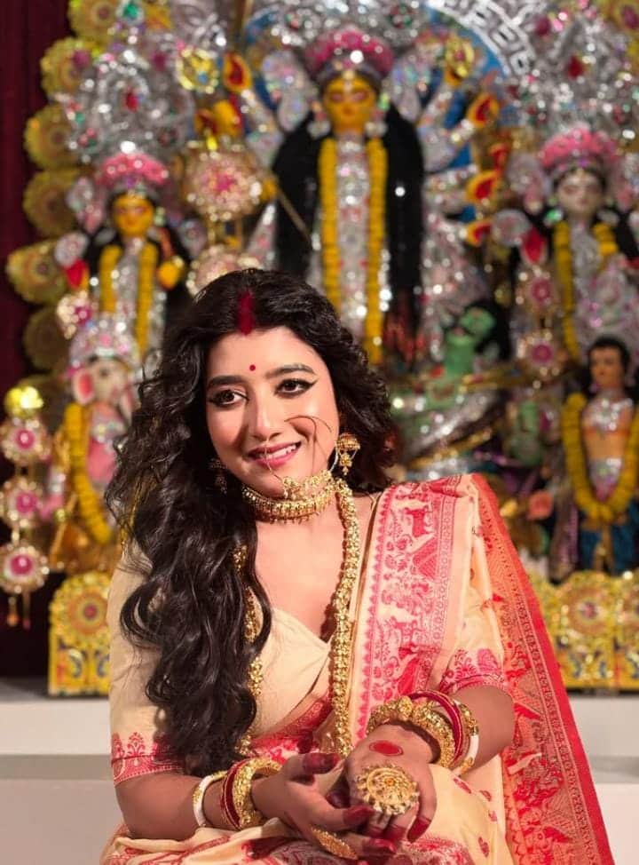 পরনে লাল পাড় শাড়ি, সঙ্গে শোভা বাড়াচ্ছে সোনার গয়নার ঝলমলানি। পিঠে একঢাল খোলা চুল, বড় নথ এবং টানা কাজল-কালো চোখেই অপরূপা হয়ে উঠেছেন পর্দার ‘রাই’ ওরফে আরাত্রিকা। অষ্টমীর অঞ্জলি হোক অথবা দেবীর বরণ, এই সাজের জৌলুসে আপনিই হয়ে উঠবেন নজরকাড়া। 