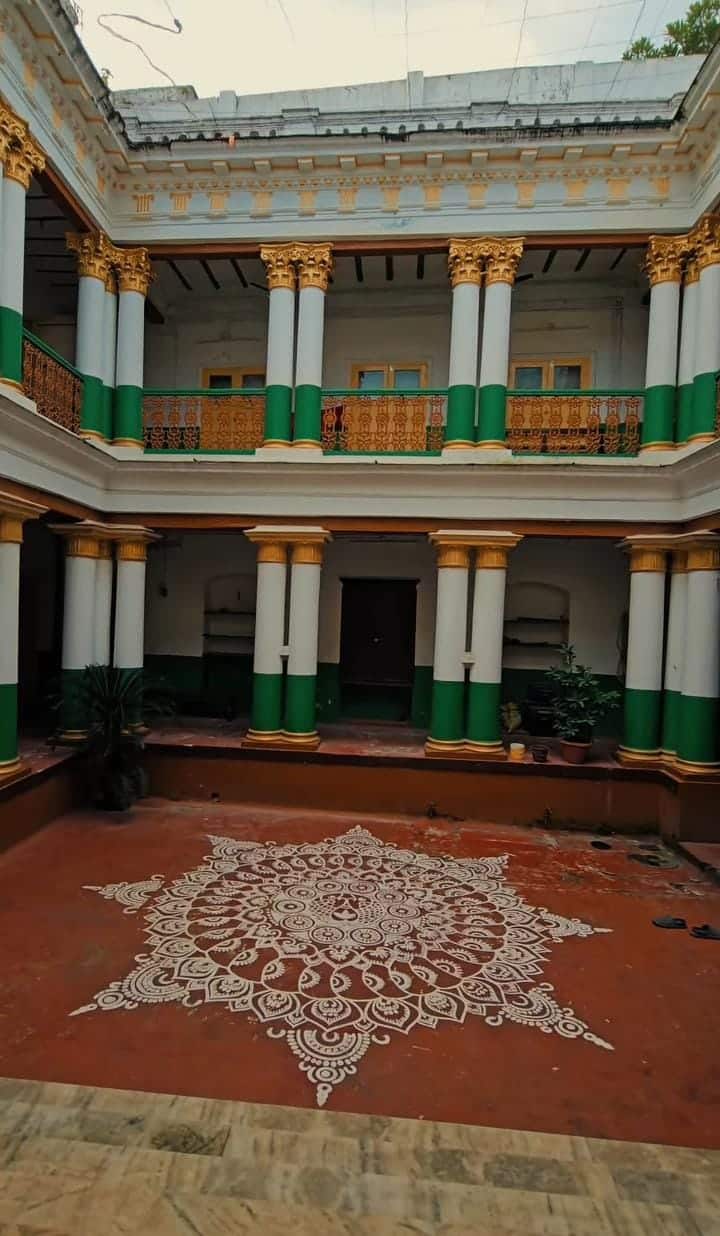  এই বাড়ির ঠাকুরদালানে পা রাখলে মনে হয় যেন ইতিহাসের পাতা উল্টে দেখা হচ্ছে। সোনালি নকশার সেই ঠাকুরদালান, লাল মেঝে আর তাতে আঁকা বিশাল আলপনা—সব কিছু মিলে এক অন্য রকম আবহ তৈরি করে এই বাড়ি। 
