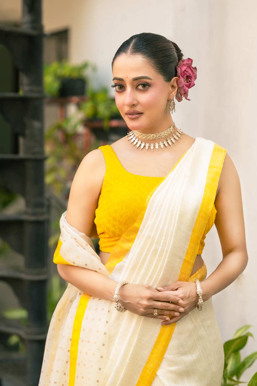 অনুপমের মতে, হলুদ ছাড়া আবার বাঙালির উৎসব পূর্ণ হয় না কি! একটি সাজে হলুদ রং তো থাকবেই। তাই রাইমাকে তিনি সিল্ক মটকা মসলিনের শাড়ি পরালেন হাতকাটা ব্লাউজ়ের সঙ্গে। ছিমছাম জেল-ব্যাক খোঁপা বাঁধা হয়েছে রাইমার চুলে। তার সঙ্গে মাথায় গুঁজে দেওয়া হয়েছে পদ্মফুল। পয়লা বৈশাখের আমেজ স্পষ্ট হয়ে গেল ফুলের এই সাজেই। বেল-জুঁই তো অতি ব্যবহৃত। সেখানে পদ্ম যেন বিশেষ ভাবে নজর কাড়বে ভিড়ের মাঝেও। তেমনই নজরকাড়া সাজ পছন্দ অভিনেত্রীরও। দু’হাতে মকরবালা, রুপোলি লিচুকাটা হাঙরমুখ বালা হাতে, গলায় নকশা করা ঠোকাইয়ের চোকার। সঙ্গে কপালও সেজেছে টিপে।