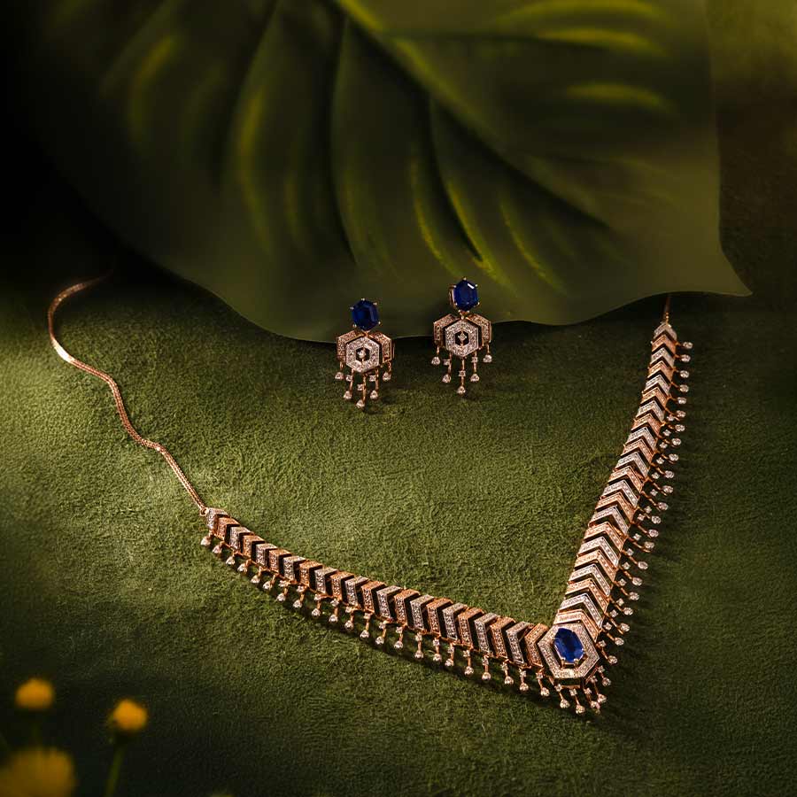DGN-D000817434, DTGN-D000817435 - ক্লাসিক নকশার আধুনিক রূপে তৈরি এই ১৪ ক্যারেট রোজ় গোল্ডের নেকলেসে ৩.১৬ ক্যারেট হিরে বসানো আছে, যা গাঢ় নীল পাথরের ছোঁয়ায় আরও আকর্ষণীয় হয়েছে। এর সঙ্গে রয়েছে ০.৬ ক্যারেট হিরে বসানো কানের দুল, যা একই নকশাকে বজায় রেখে পুরো সেটটিকে করেছে অনন্য।