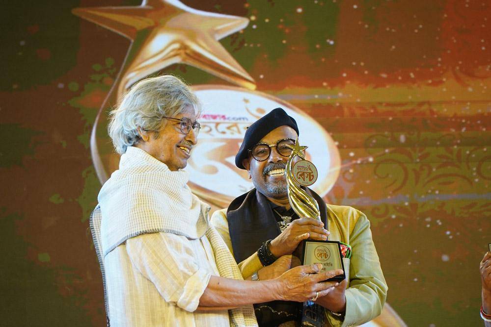 আনন্দবাজার ডট কমের ২০২৫ সালের ‘বছরের বেস্ট’ অনুষ্ঠানের মঞ্চে পরেশ মাইতির হাতে পুরষ্কার তুলে দিচ্ছেন যোগেন চৌধুরী।