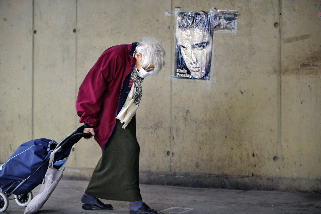 An elderly woman drags a shopping trolley, backdropped by an Elvis Presley poster, at a market place in Bucharest, Romania, Tuesday, April 14, 2020, during the two hour daily interval when people over 65-years old are allowed to leave their homes for essential shopping, a measure imposed by authorities to limit the spread of the COVID-19 infections. According to the emergency state regulations, people over 65 years old are only allowed to leave their homes for two hours a day, which many of them consider impractical as it leads to overcrowded shops and market places, increasing the risk of contamination.