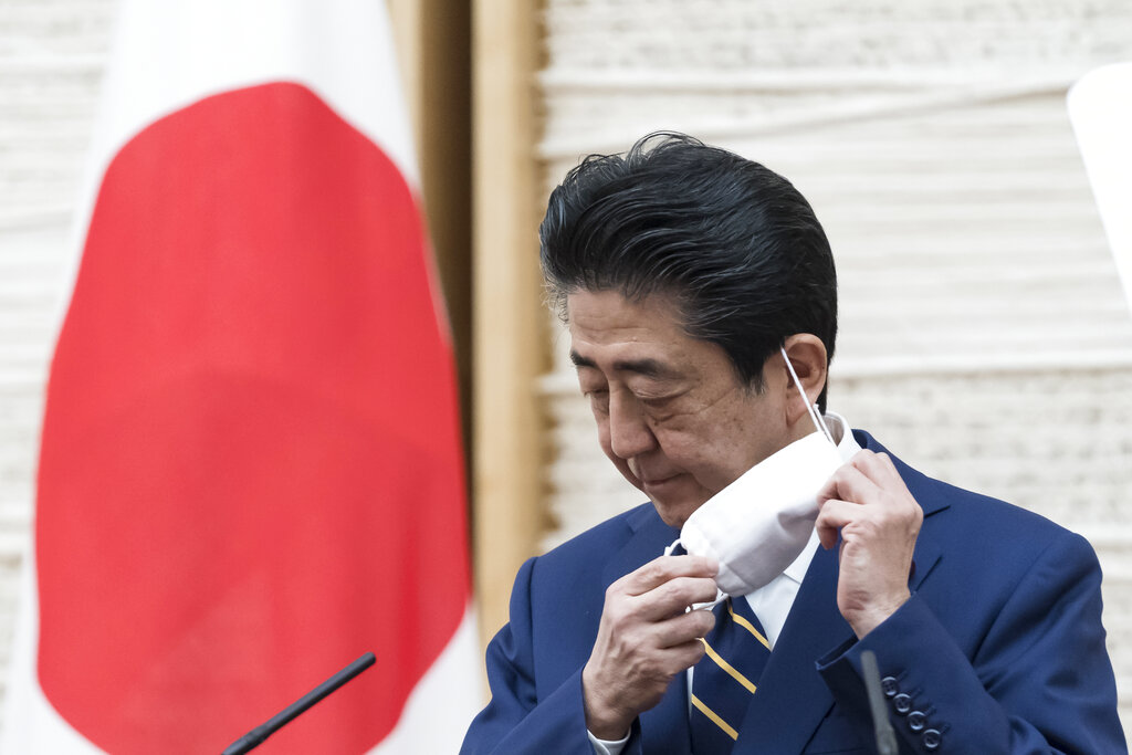 Japan's Prime Minister Shinzo Abe removes his face mask during a press conference at the prime minister's official residence Tuesday, April 7, 2020, in Tokyo. Abe declared a state of emergency for Tokyo and six other prefectures to ramp up defenses against the spread of the coronavirus.
