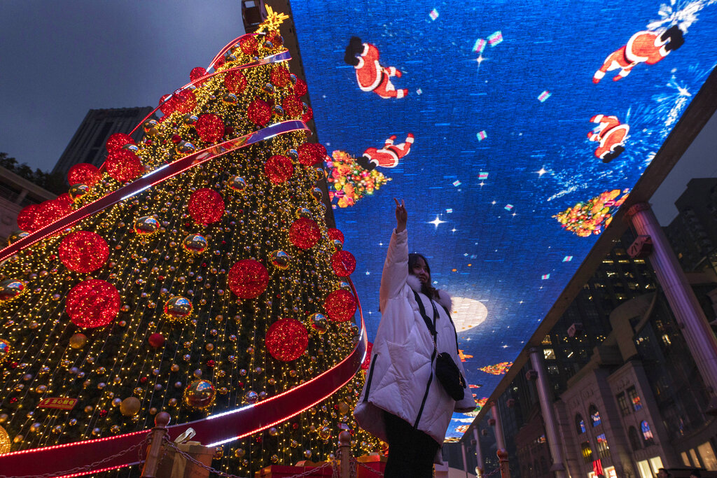 A woman poses for photos near a giant Christmas tree and Christmas themed display during Christmas Eve in Beijing on Tuesday, Dec. 24, 2019.